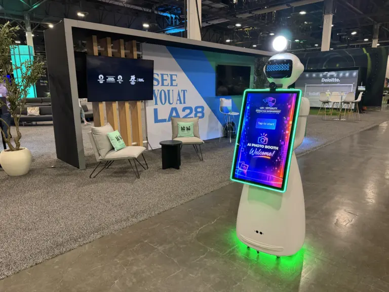 Los Virtuality AI photo booth robot with its Welcome screen beside the Deloitte lounge and branded sport simulator at the Venetian Expo, Las Vegas