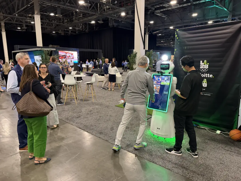 Guest checking AI sports portraits on the Deloitte branded AI photo booth robot screen next to the LA28 backdrop, Venetian Expo, Las Vegas