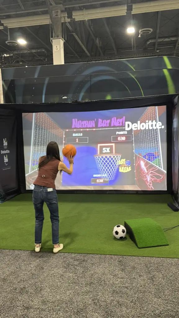 Guest shooting a basketball at the Deloitte-branded sport simulator screen at the Venetian Expo, Las Vegas
