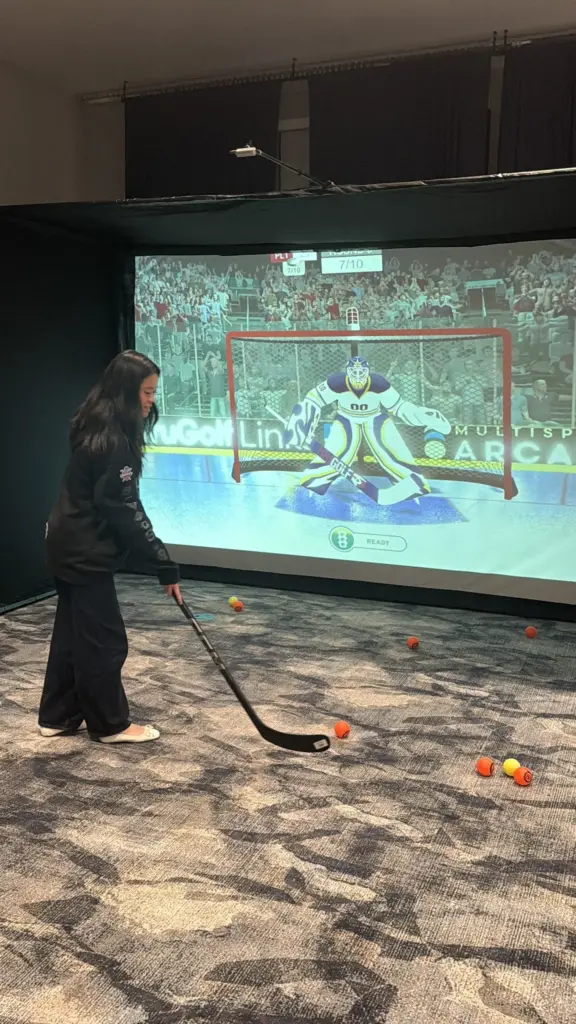 Guest lining up a shot at the hockey simulator screen with a virtual goalie