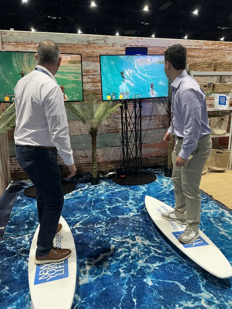 Two attendees surfing on New York Life Investment Management branded boards over an ocean-print floor at LPL Focus 2026, San Diego
