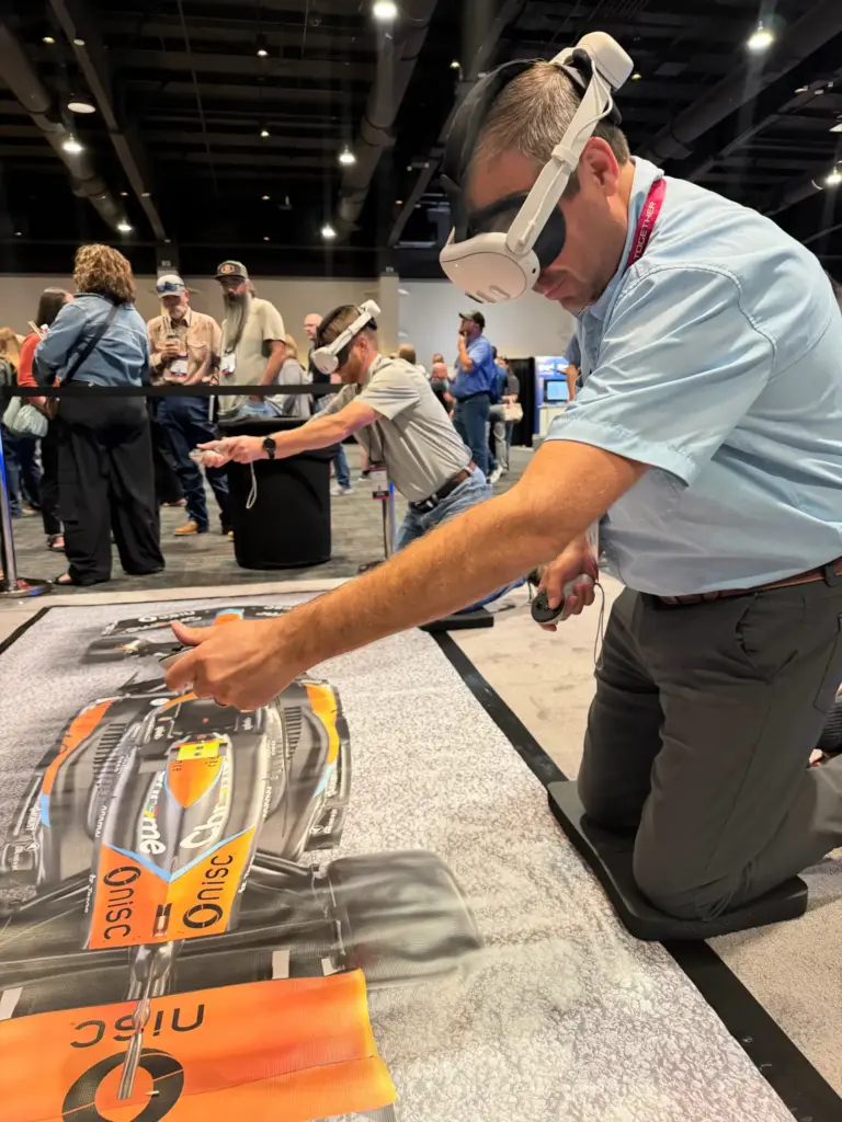 Attendee in a VR headset changing a tire in the pit stop challenge on the pit lane mat at NISC Member Information Conference 2026, MGM Grand Marquee Ballroom
