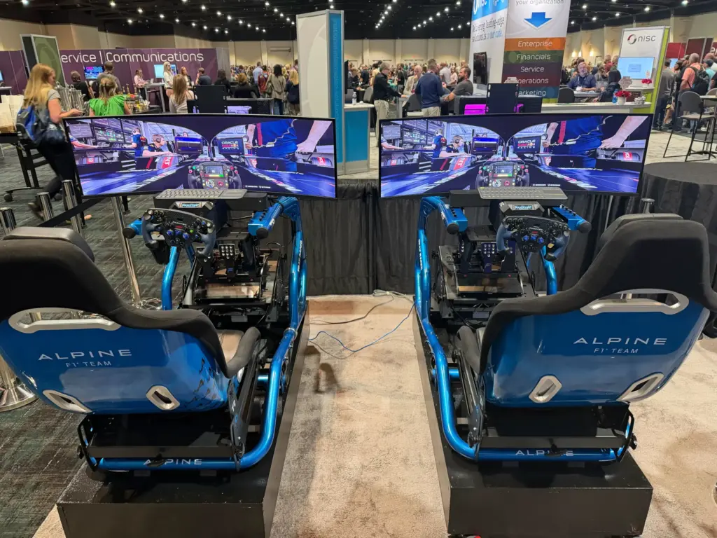 Two professional racing simulators with curved screens and racing wheels set up on the NISC Member Information Conference 2026 expo floor, MGM Grand, Las Vegas