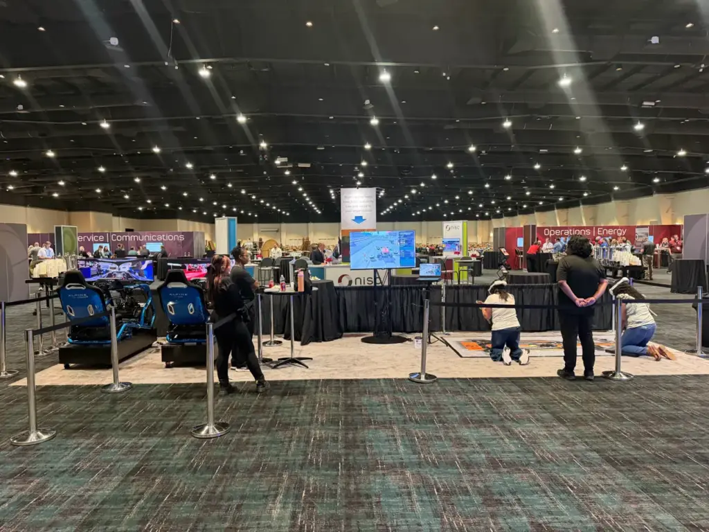 Racing simulators and the VR pit stop challenge side by side next to the NISC booth at the Member Information Conference 2026, MGM Grand Marquee Ballroom, Las Vegas