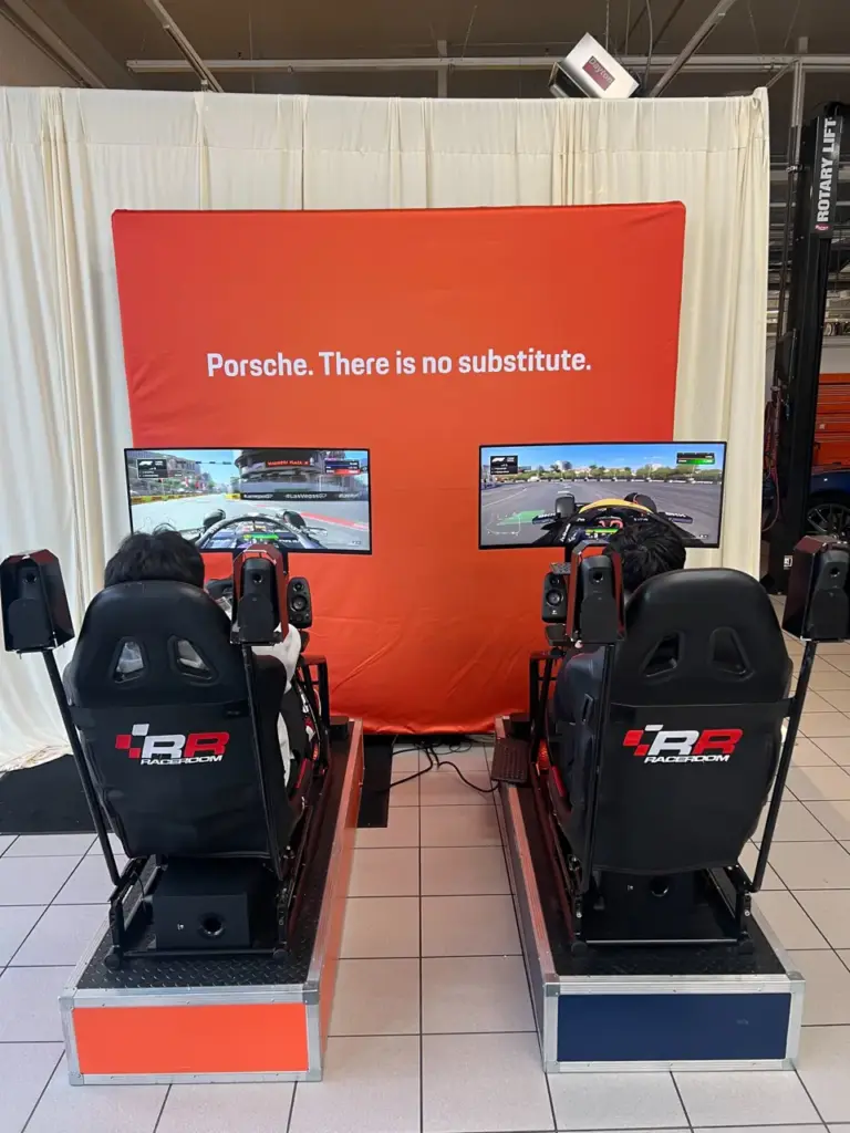 Two racing simulators in front of a Porsche backdrop at a Porsche dealership client event in San Francisco