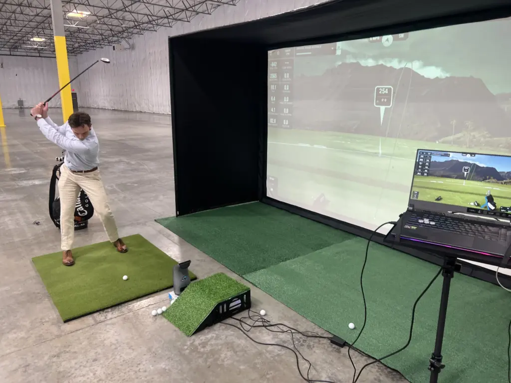 Guest swings at a staffed golf simulator during a Prologis company event in a Renton, WA warehouse
