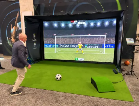 Guest kicking a ball at a soccer simulator rental with a goalkeeper on the big screen
