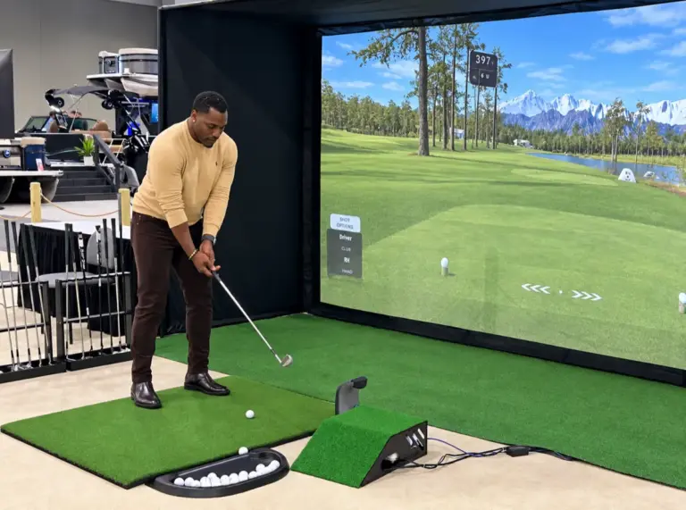 Guest swinging a club at a golf simulator rental in front of a large course screen