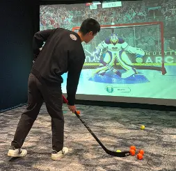 Guest taking a shot at a hockey simulator rental with a virtual goalie on screen
